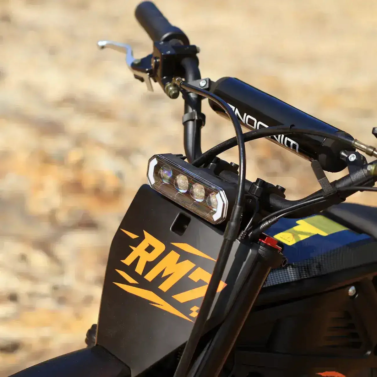 Close-up of RM7 dirt bike handlebars and LED headlight on off-road terrain