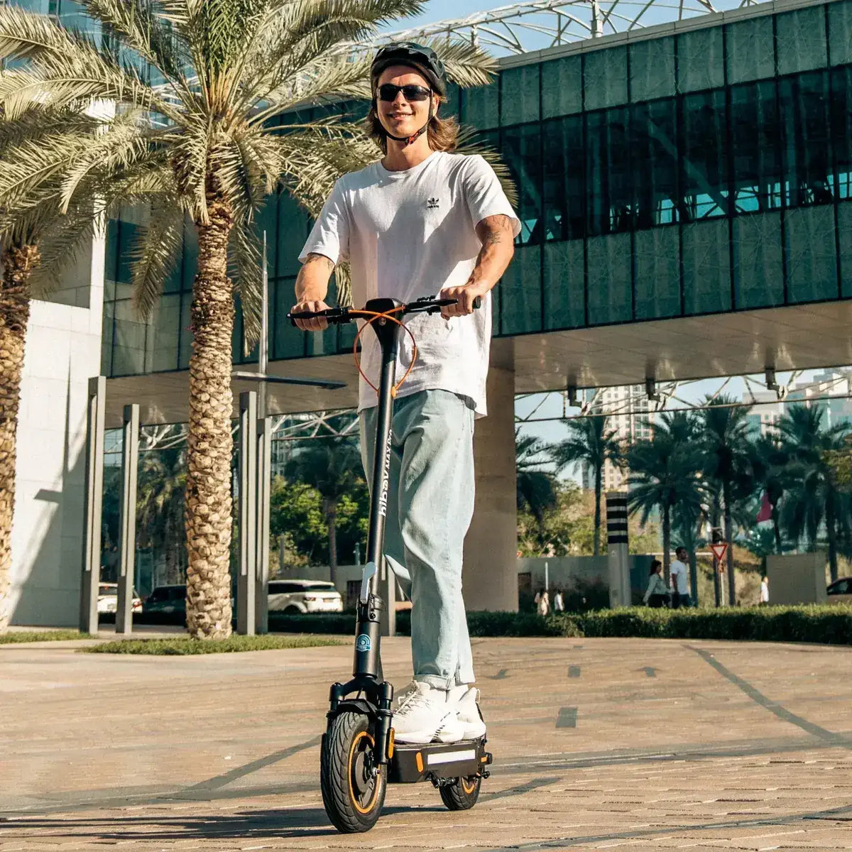 Man riding an electric scooter outdoors in a city with palm trees and modern buildings