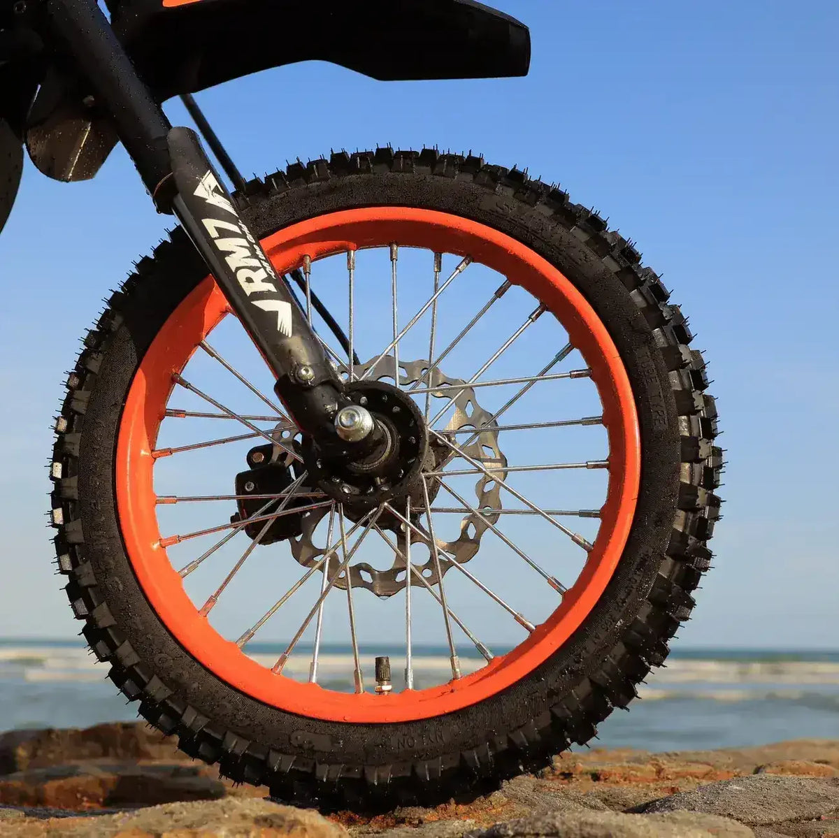 Close-up of a dirt bike front wheel with knobby tire and orange rim on rocky terrain