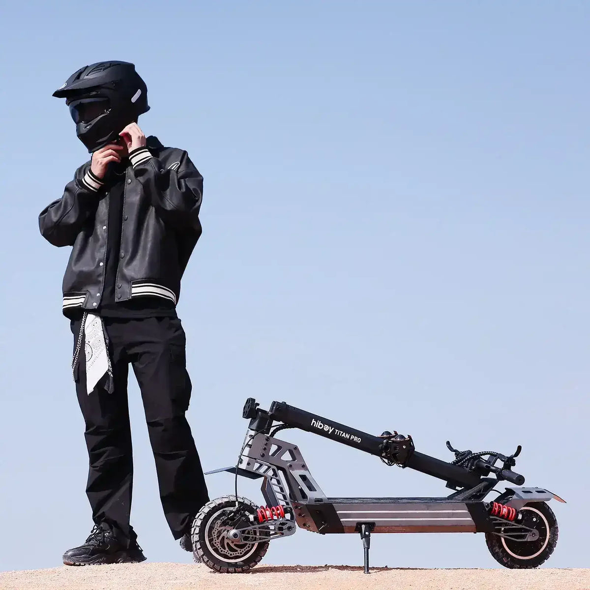 Person in black gear and helmet standing beside a folded off-road electric scooter outdoors