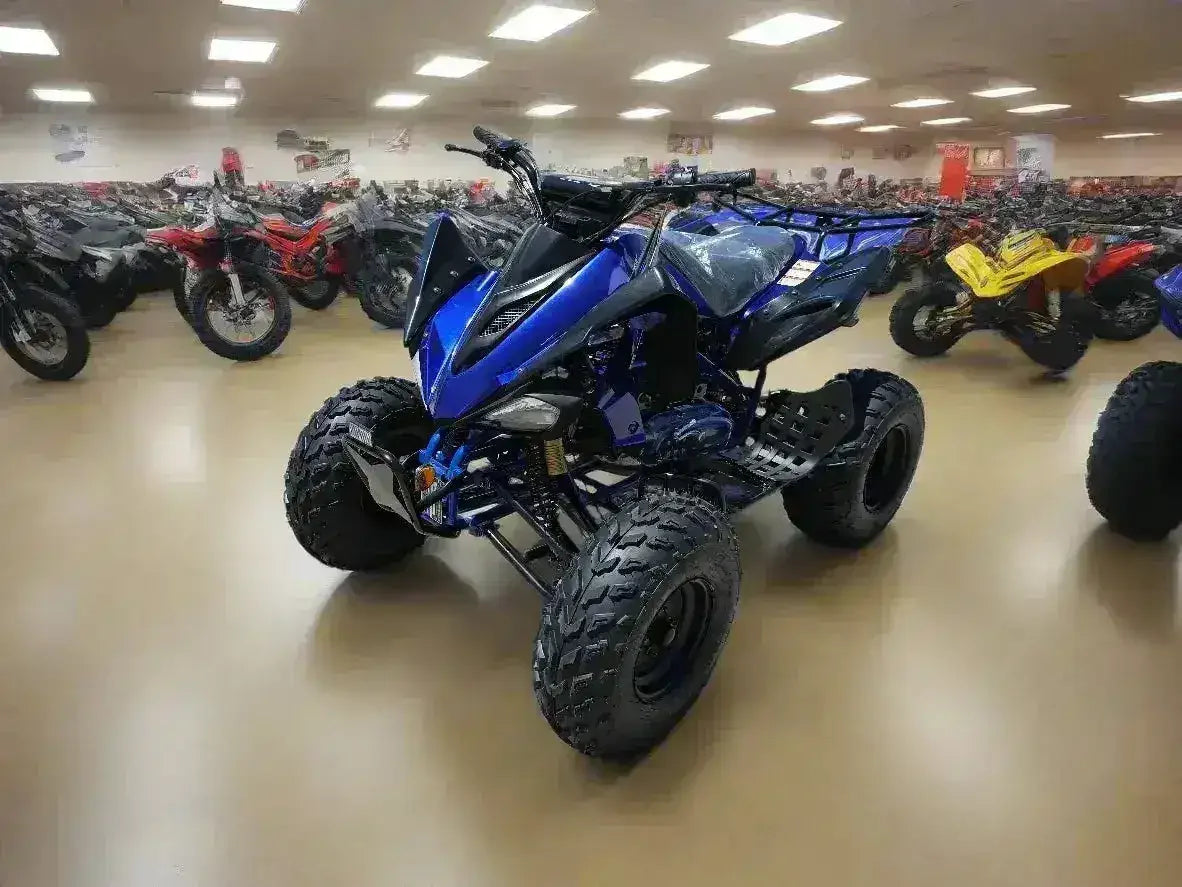 Blue all-terrain ATV with large tires on showroom floor surrounded by other quad bikes