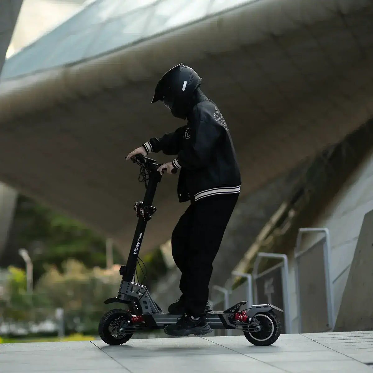 Person riding an electric scooter outdoors wearing a helmet and black jacket
