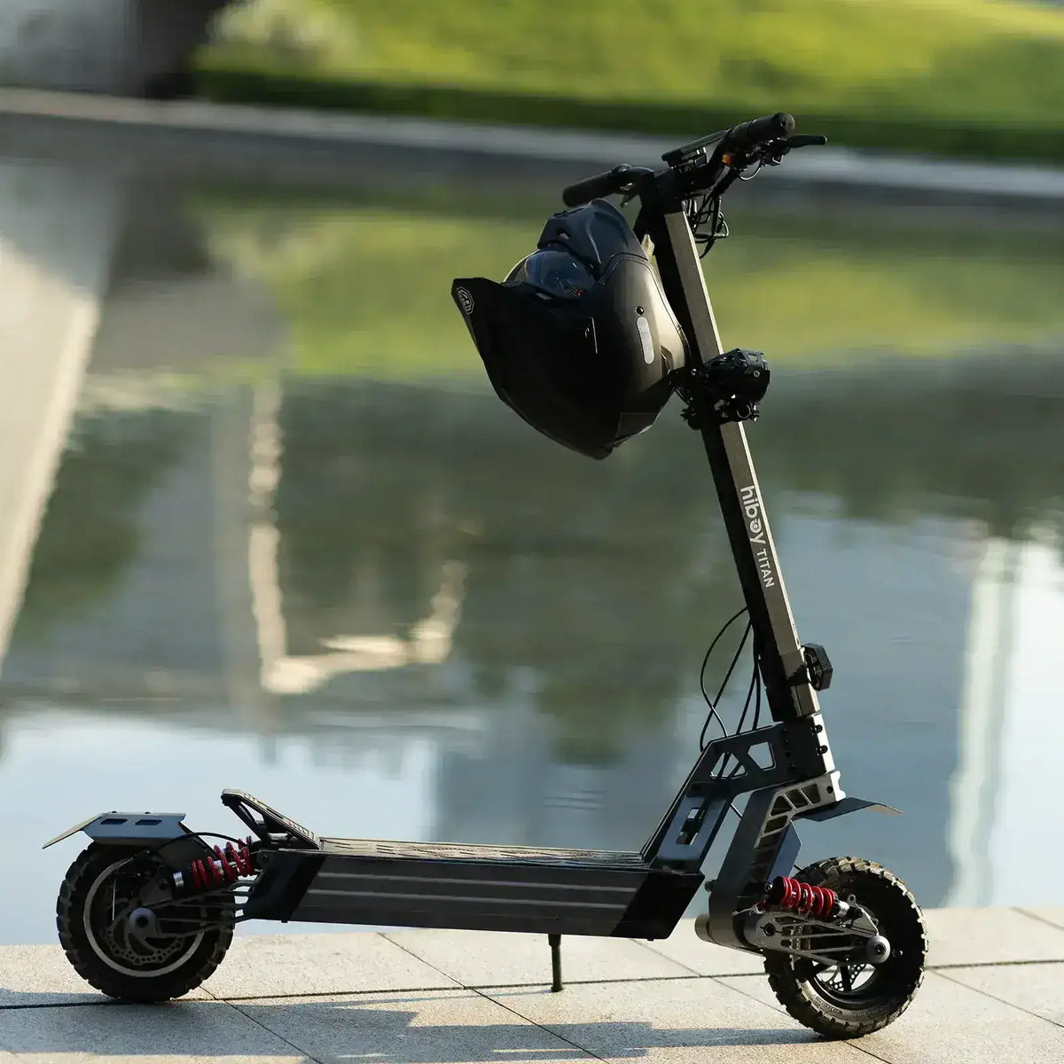 Black off-road electric scooter with helmet parked by a reflective water surface