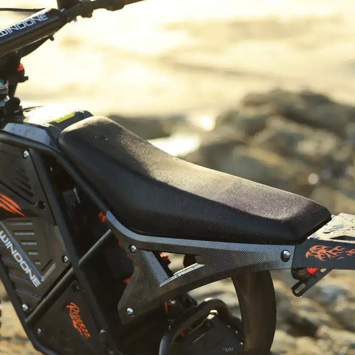 Close-up of an electric dirt bike seat and frame with black and orange accents outdoors