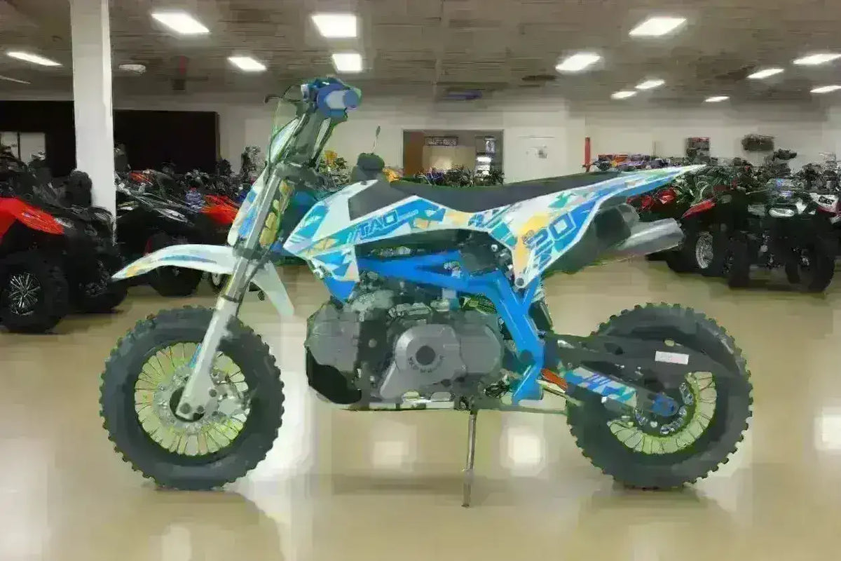 Blue 20cc dirt bike with off-road tires displayed indoors among ATVs and motorcycles