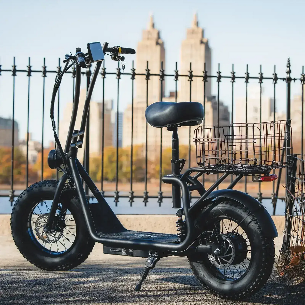 Fat tire electric scooter with rear cargo basket parked outdoors near city rail fence