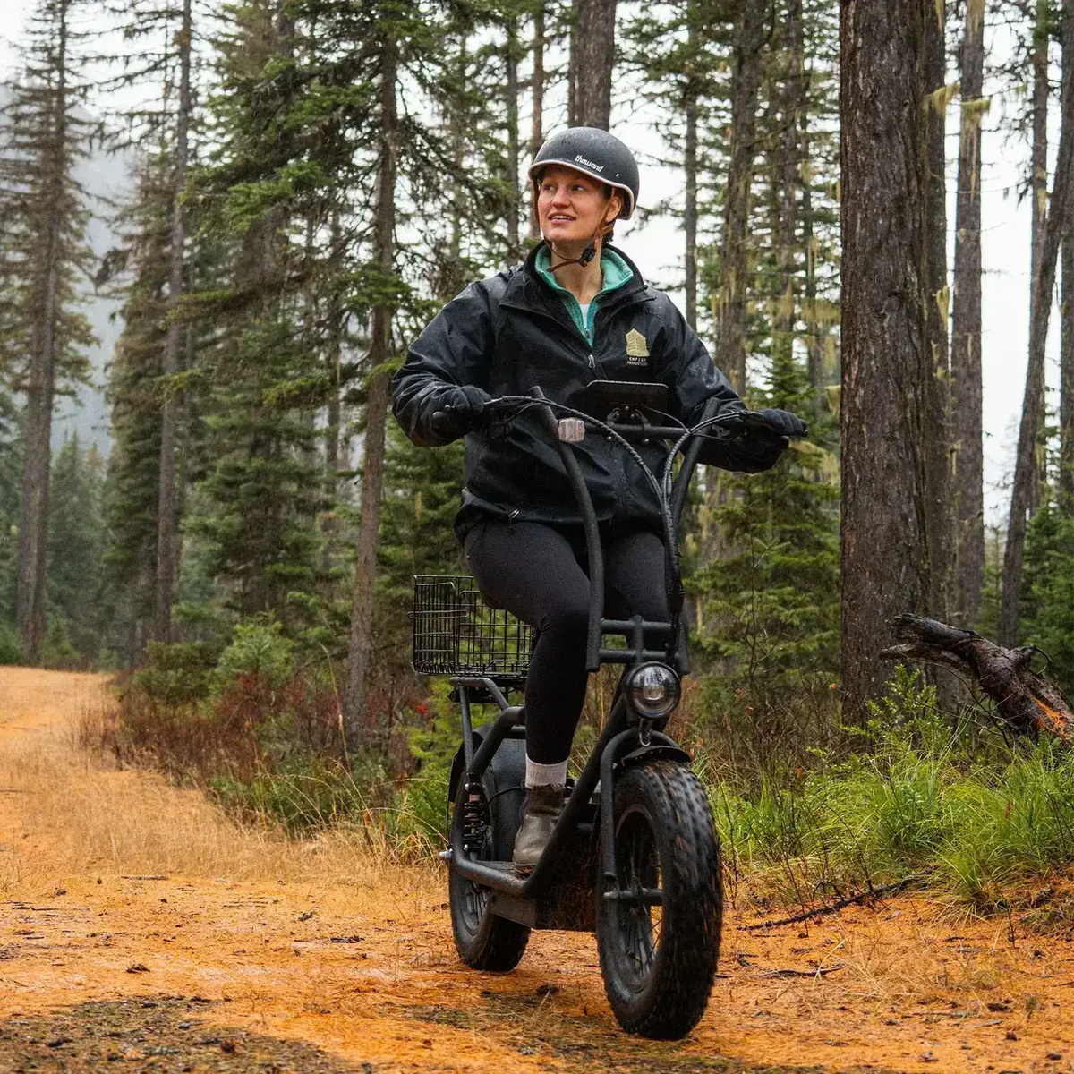 Woman riding an electric dirt bike on a forest trail, wearing helmet and outdoor clothing