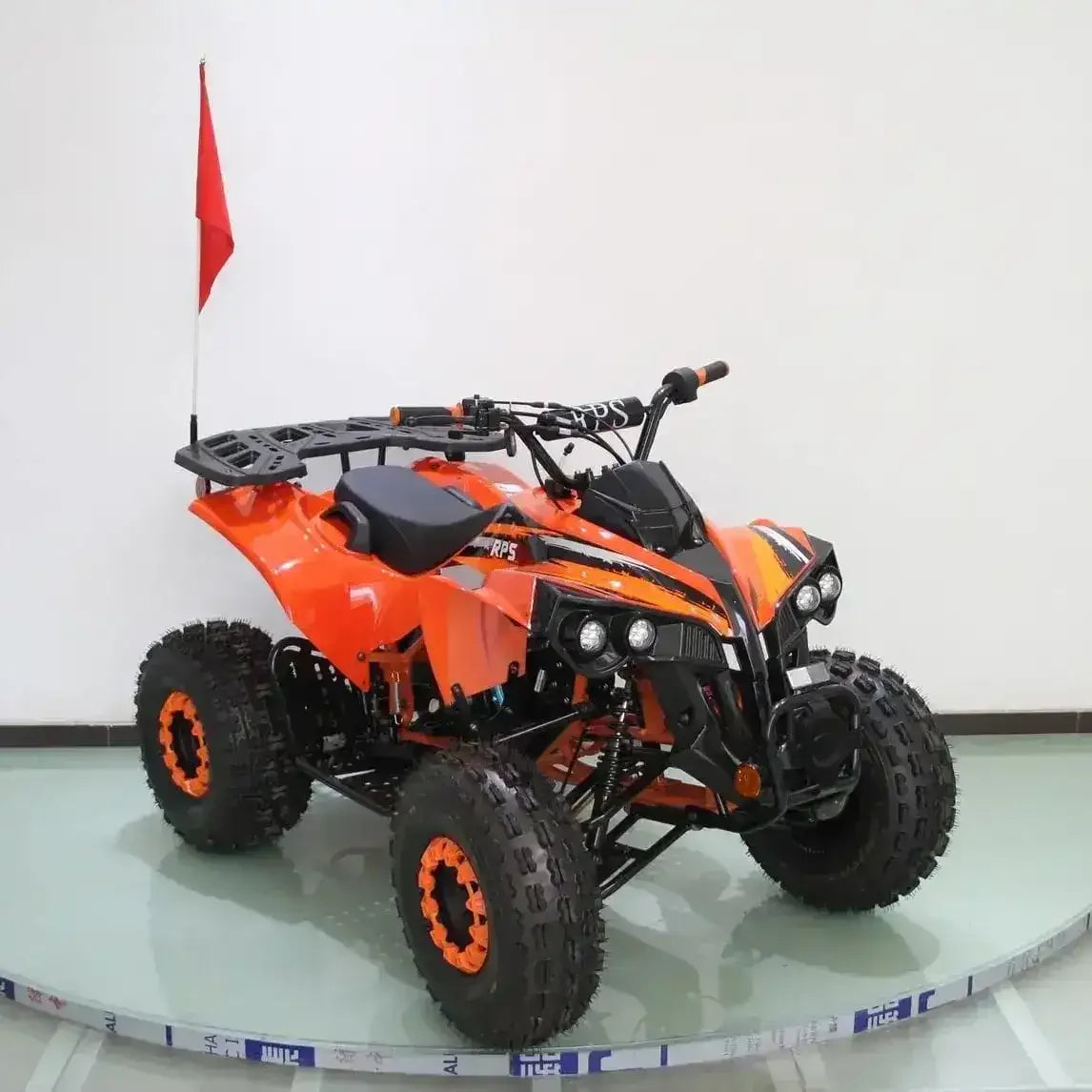 Orange 125cc ATV with off-road tires, front rack, and red safety flag in studio setting
