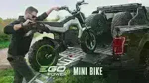Man loading electric mini bike onto a pickup truck using a ramp outdoors