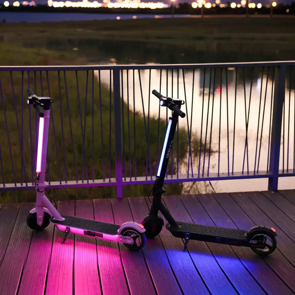 Electric scooters with colorful LED lights parked on a wooden deck at dusk by a lake.