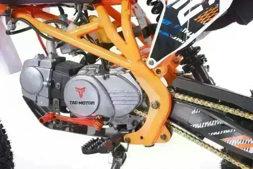 Close-up of 125cc youth dirt bike engine and frame with orange chassis and visible chain.