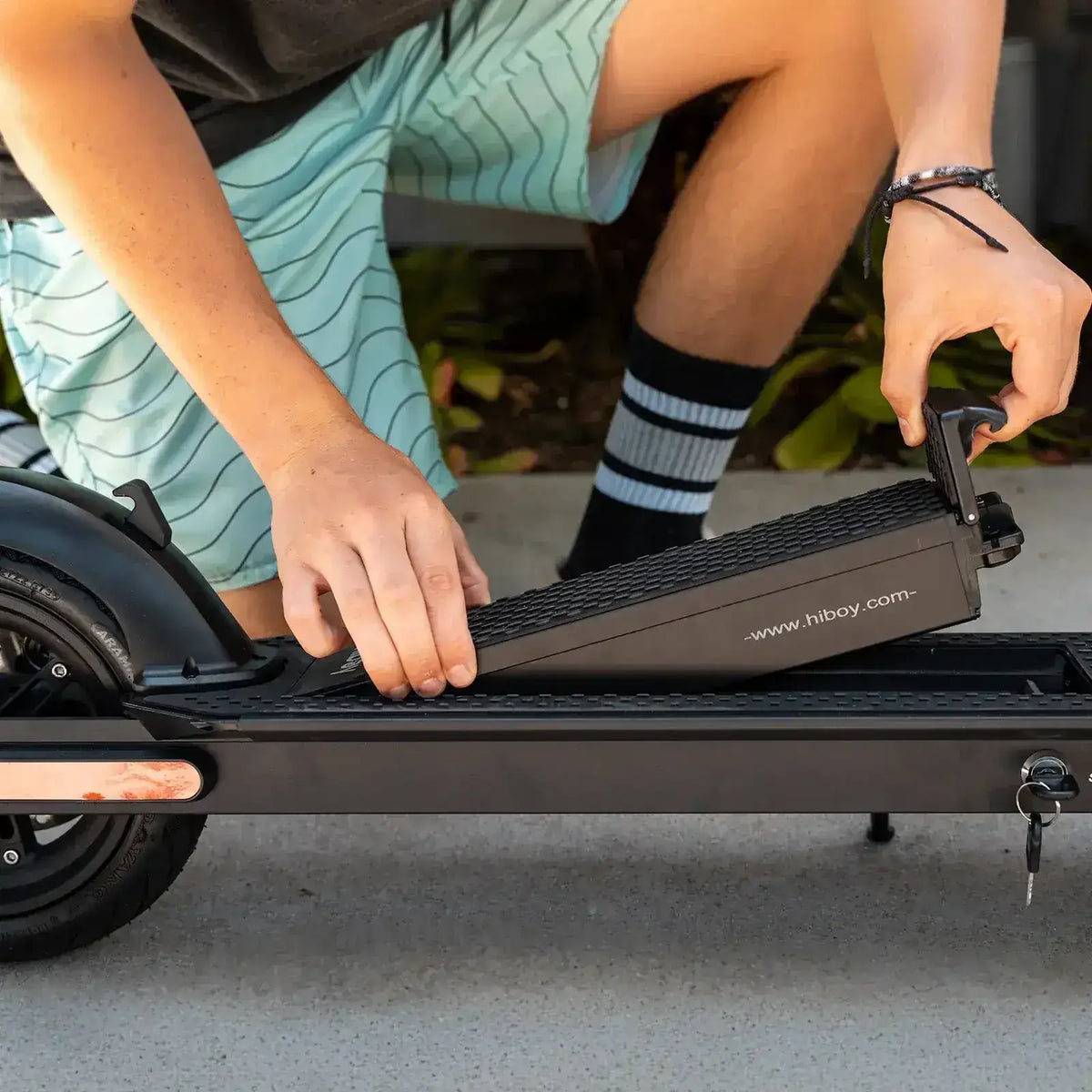 Person removing battery from electric scooter outdoors, close-up of hands and scooter deck