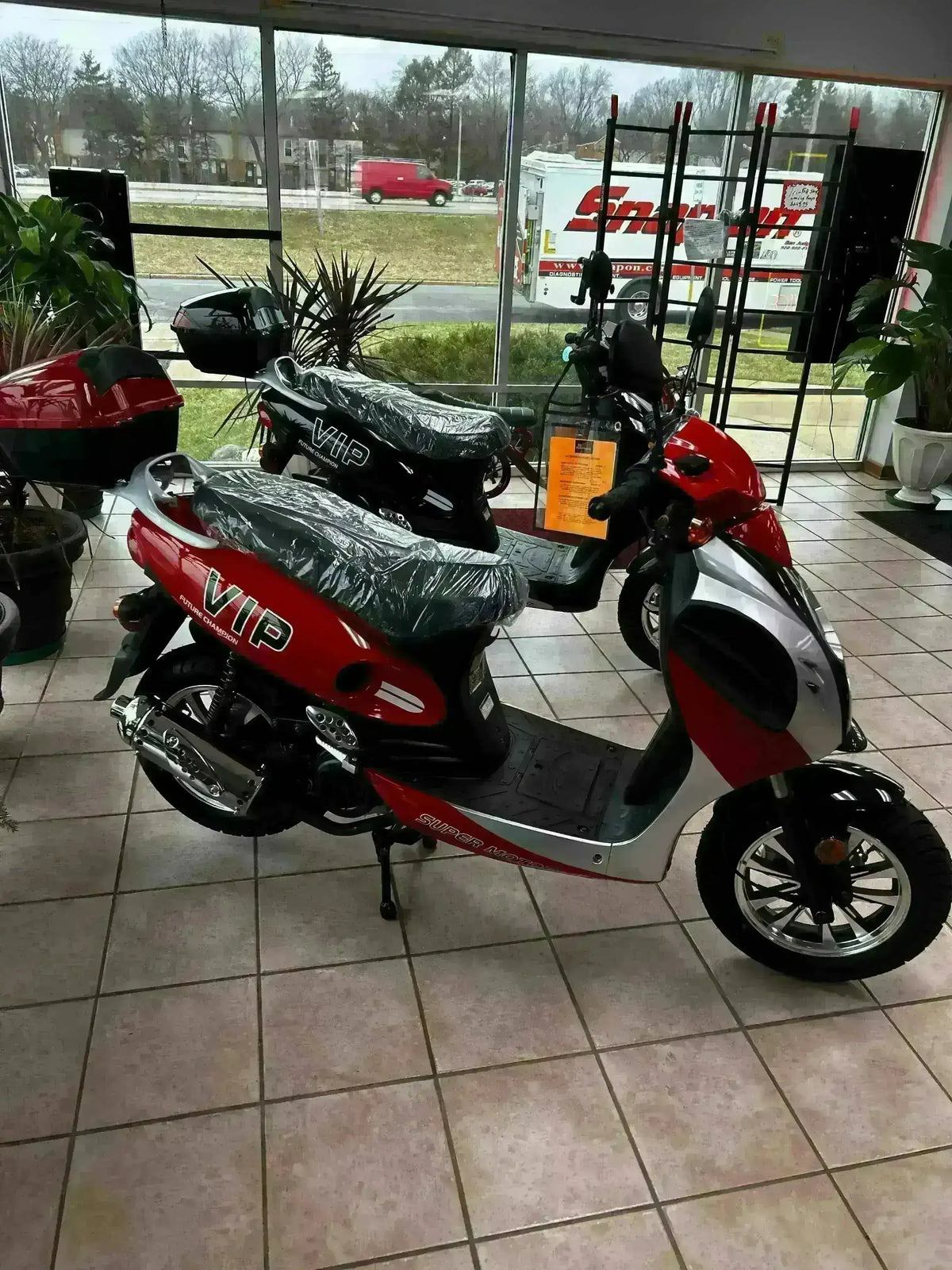 Red and black 150cc VIP scooters on showroom floor with large windows in background
