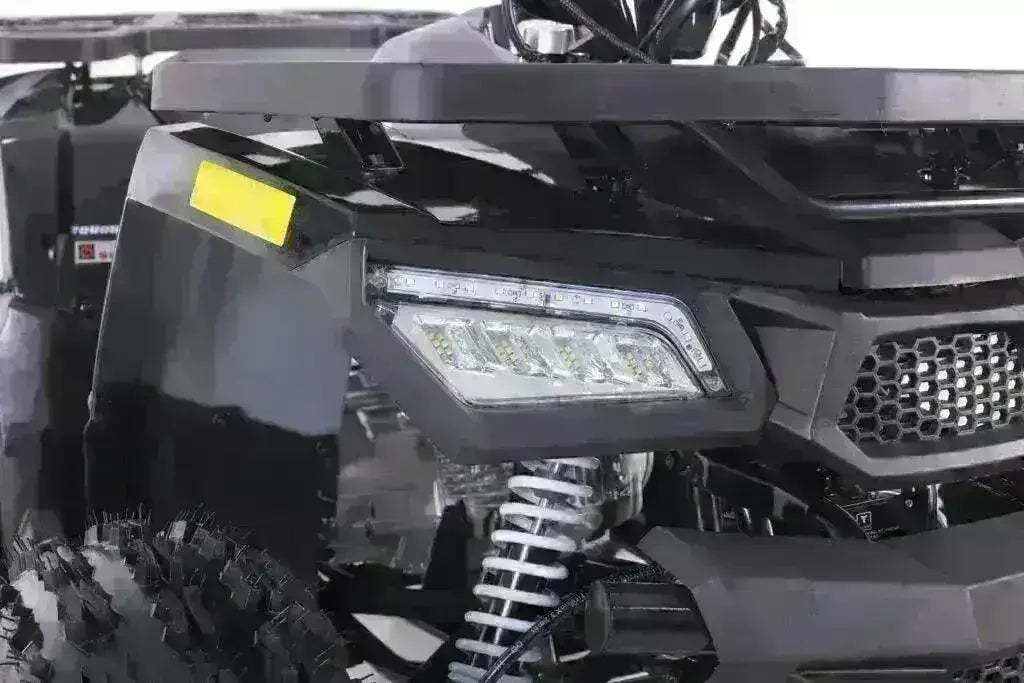 Close-up of youth utility ATV front, showing LED headlights, chunky tire, and suspension.