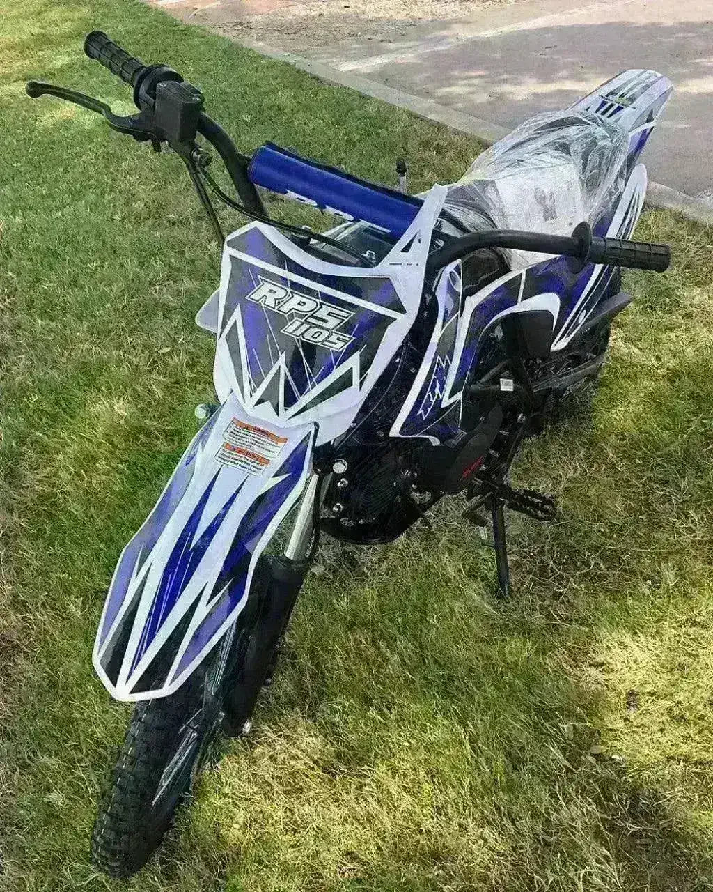 Blue and white RPS 110s dirt bike with knobby tires parked on grass