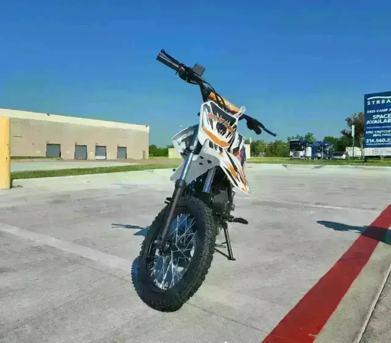 Off-road dirt bike with knobby tires and orange graphics parked on pavement under blue sky