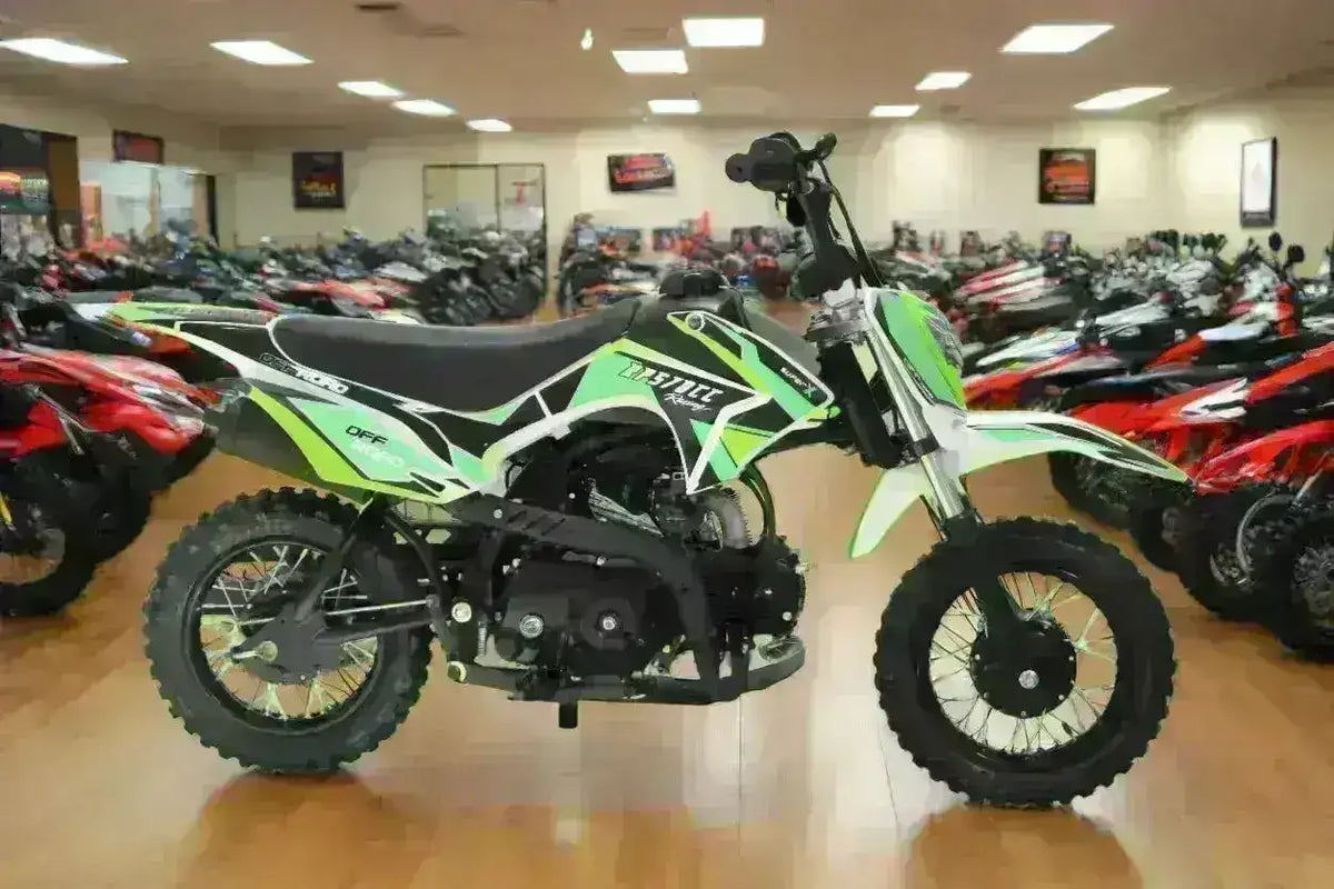 Green youth dirt bike with training wheels on showroom floor, surrounded by ATVs and bikes