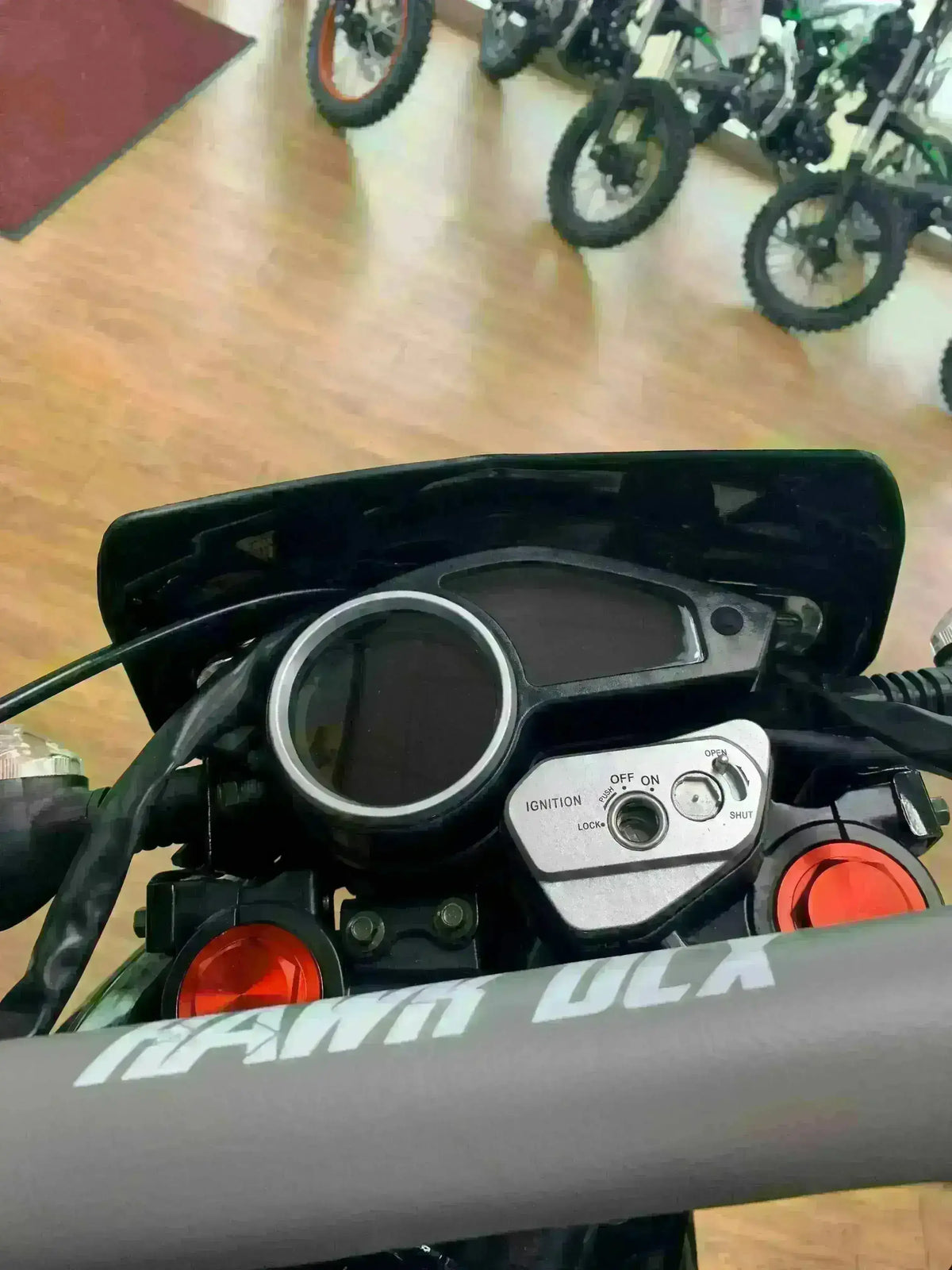 Close-up of RPS Hawk DLX 250 motorcycle dashboard and controls in showroom with dirt bikes