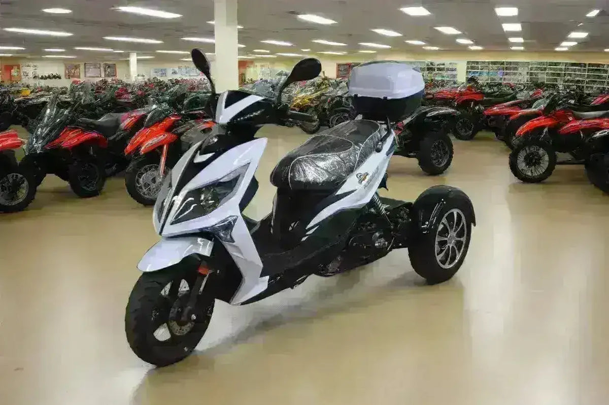 White and black three-wheeled 50cc trike scooter displayed in a showroom with ATVs