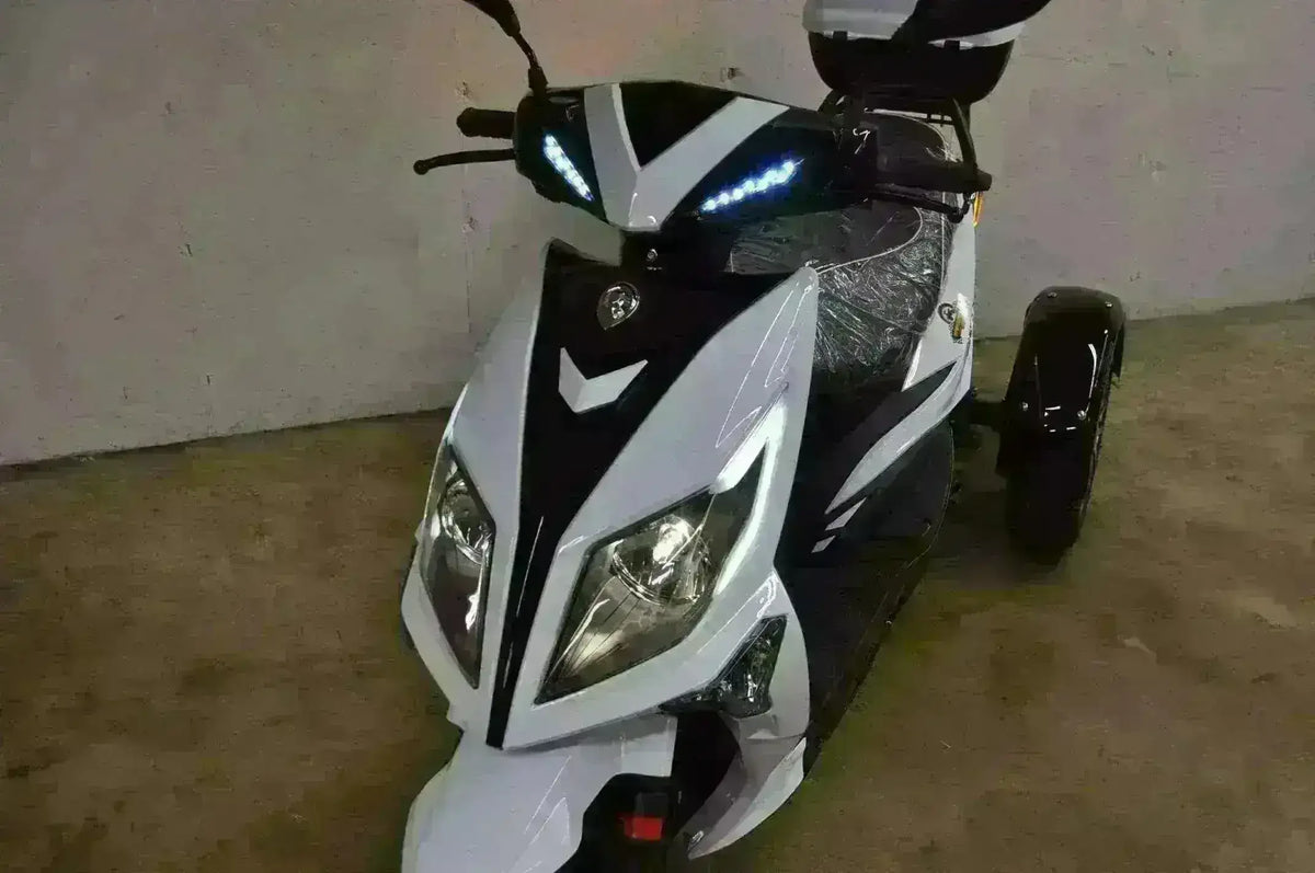 White and black three-wheeled 50cc trike scooter with LED headlights, parked indoors.