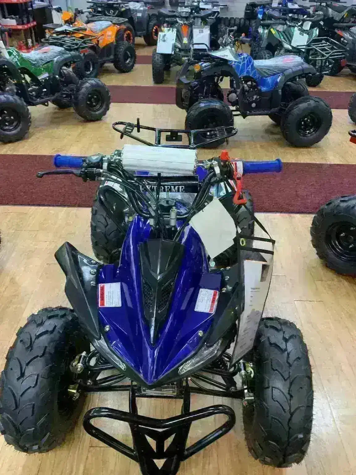 Blue youth ATV with rugged tires and black frame on showroom floor among other all-terrain vehicles