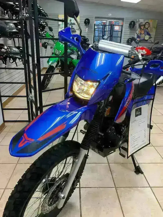 Blue dirt bike on showroom floor with off-road tires and headlight, surrounded by helmets