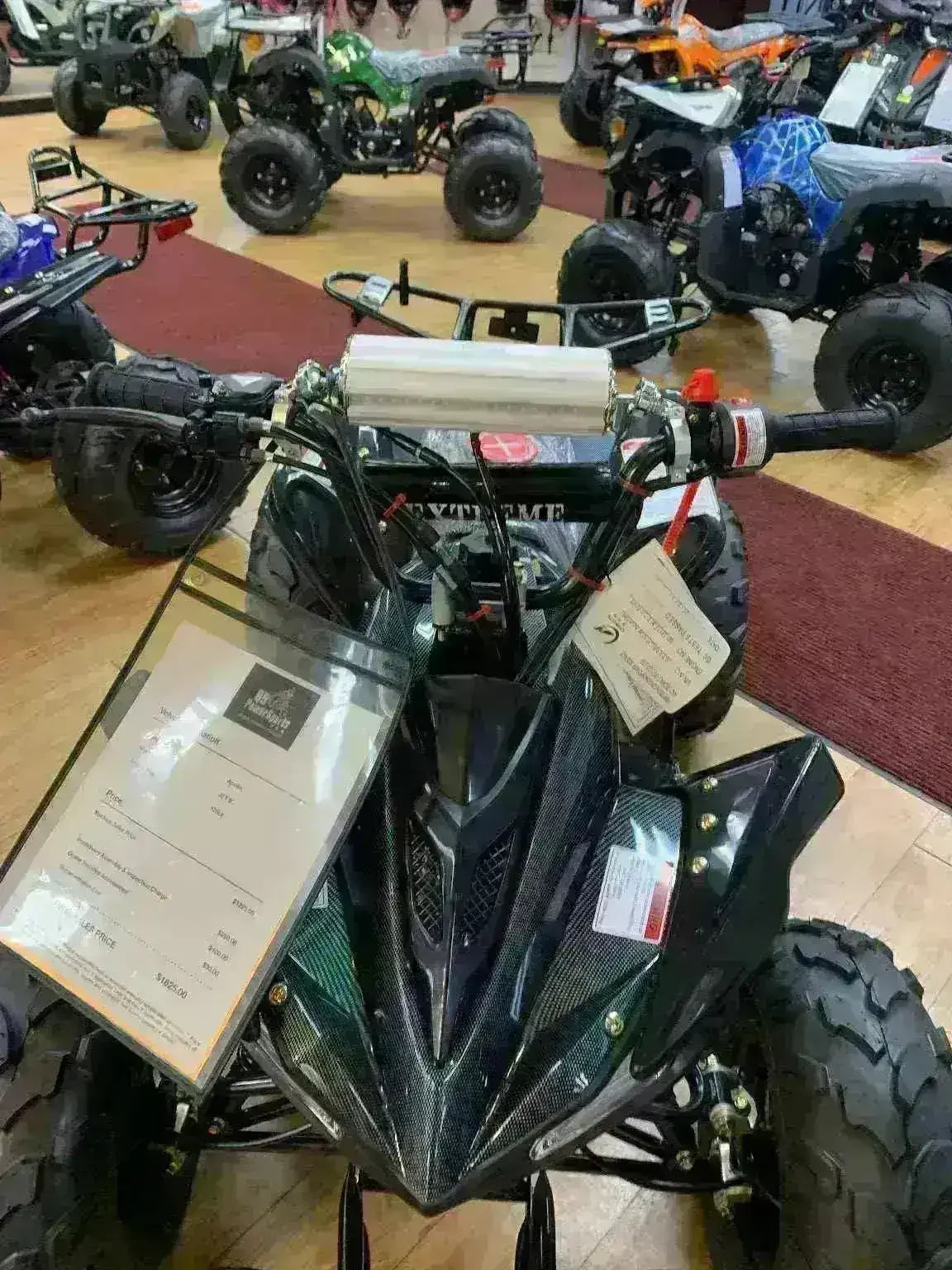 Black youth ATV with knobby tires displayed in a showroom with other all-terrain vehicles.