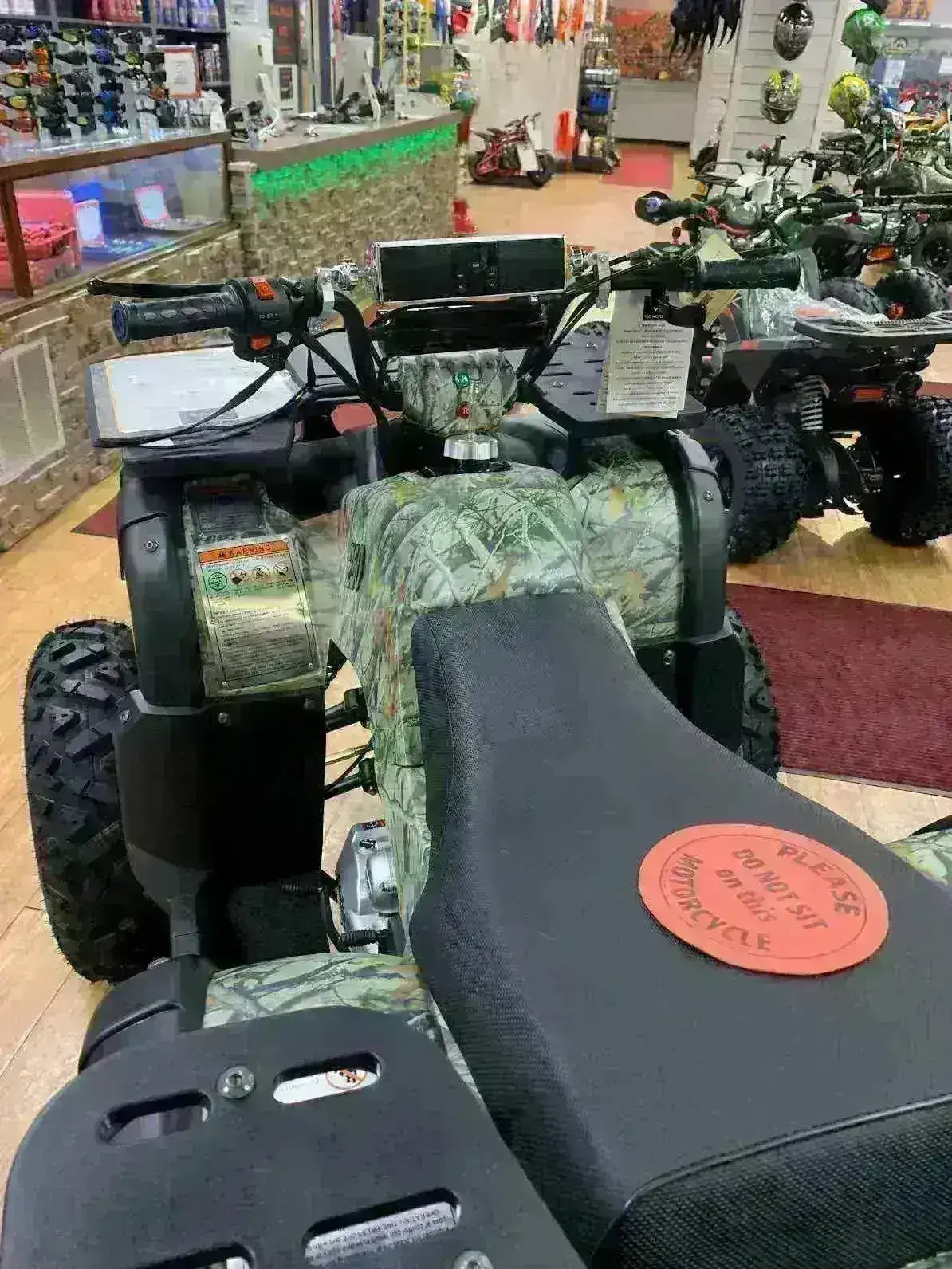 Camo ATV with universal mount Bluetooth speaker on handlebars in showroom with off-road vehicles