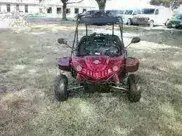 Red 2-seater 125cc go-kart parked on grass with roll cage, front view