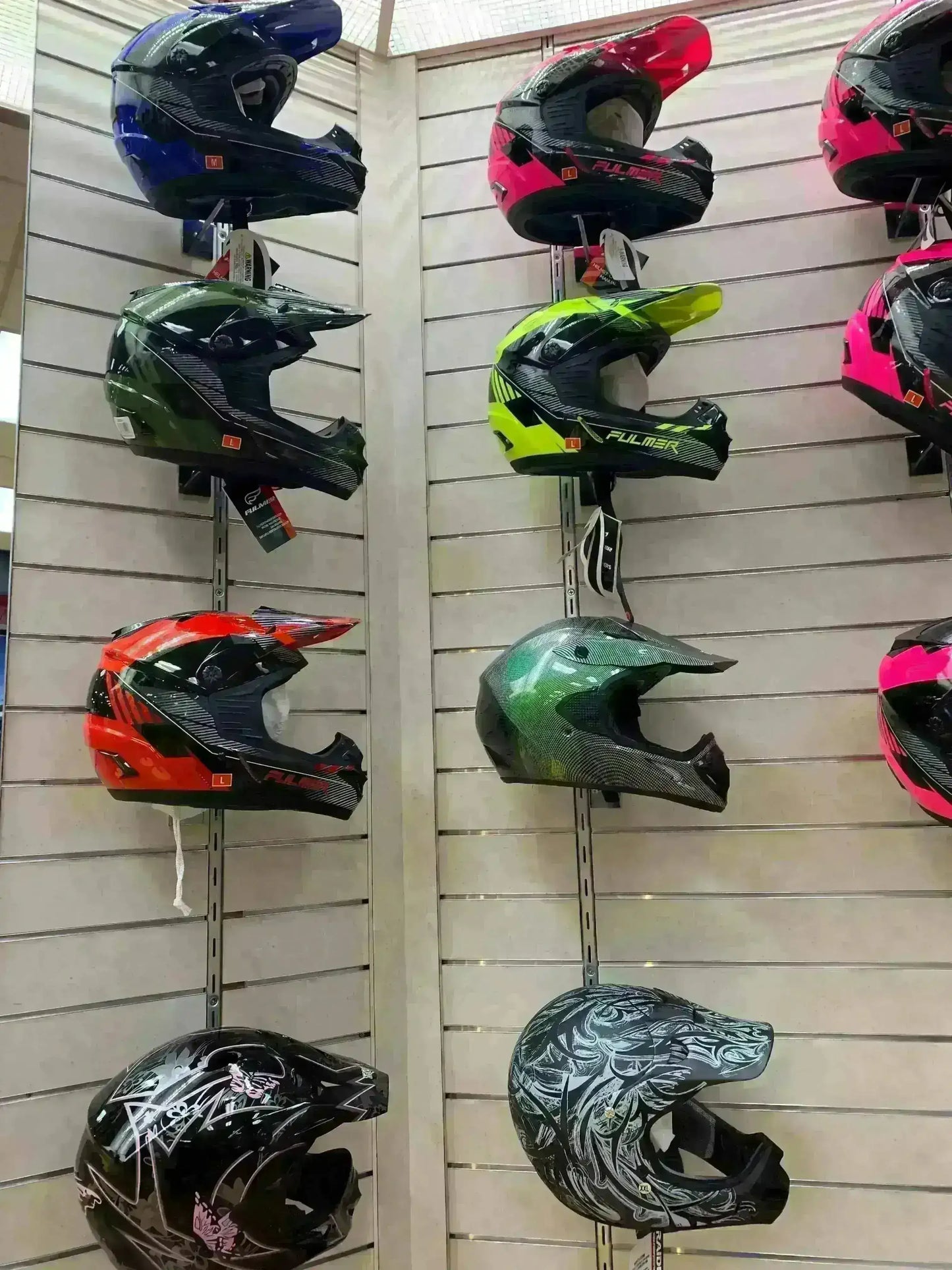 Assorted youth DOT approved motocross helmets in various colors displayed on wall.