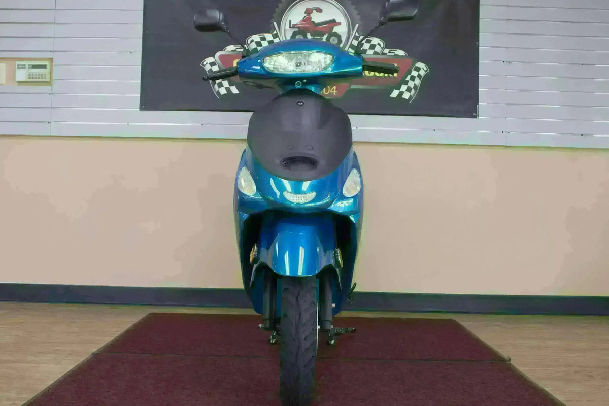 Front view of a blue 50cc scooter parked indoors, showing headlights and mirrors.