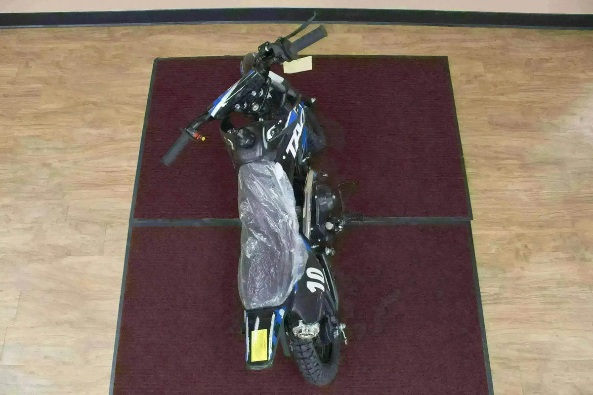 Top view of a black and blue kids 110cc dirt bike with protective seat cover indoors