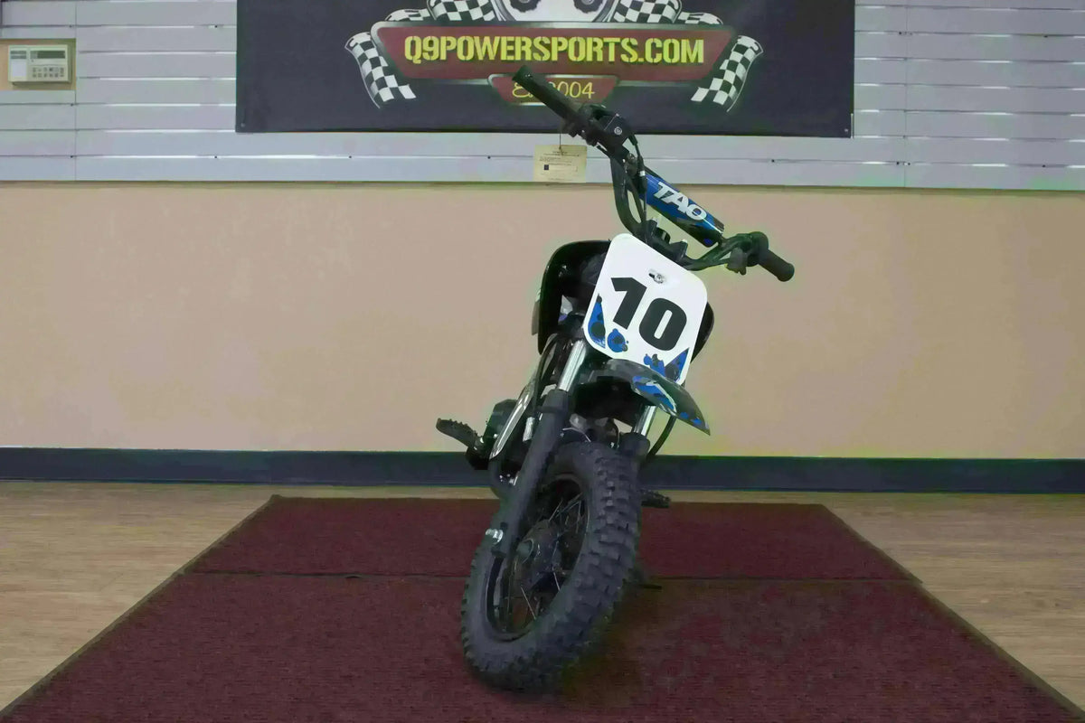 Small blue 110cc kids dirt bike with number 10 plate on display indoors