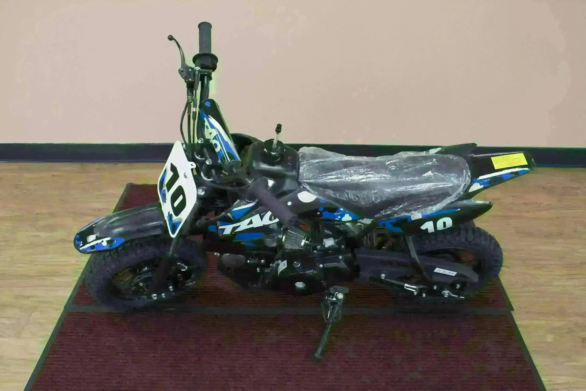 Blue 110cc kids dirt bike with black tires and number 10, displayed indoors on a red rug