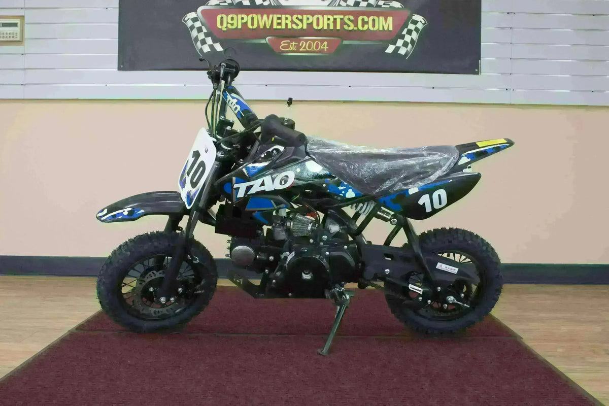 Black and blue 110cc kids dirt bike with number 10, displayed indoors on a red mat.