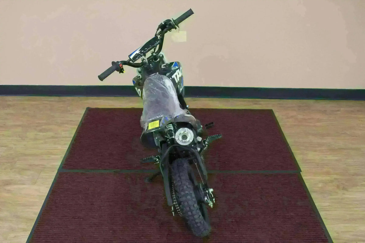 Rear view of a small 110cc kids dirt bike with knobby tires on an indoor carpet