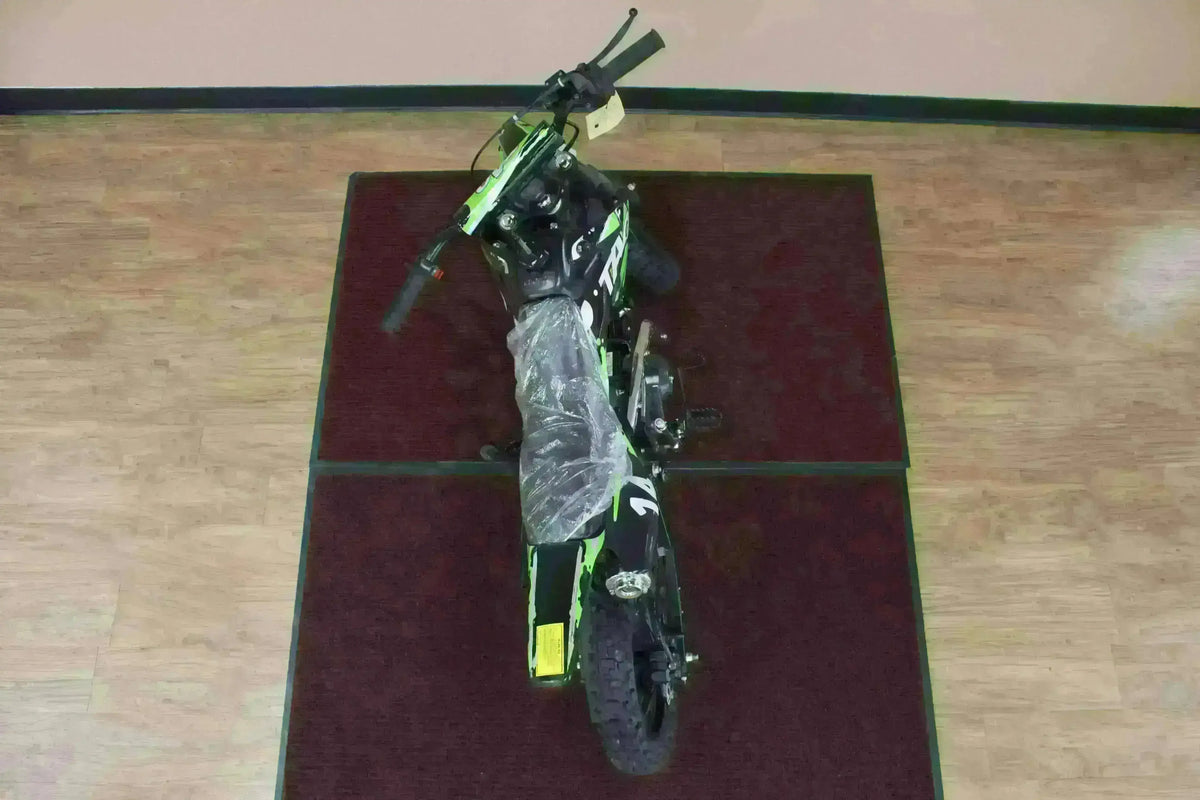 Top view of a black and green youth dirt bike with knobby tires on a showroom floor