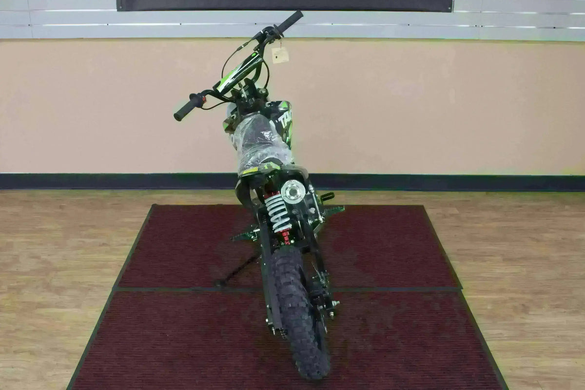Front view of a youth dirt bike with knobby tires and suspension on a showroom mat
