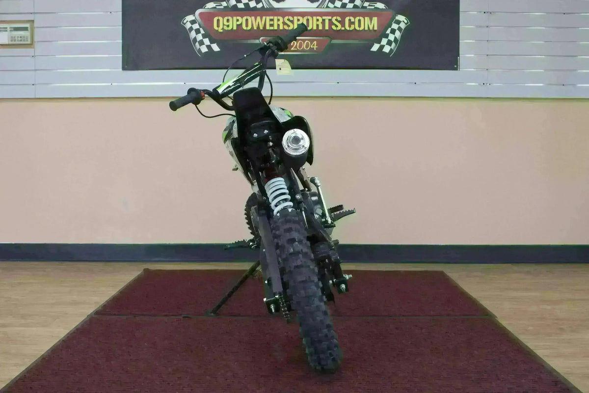 Front view of a black youth dirt bike with knobby tires on indoor showroom carpet.