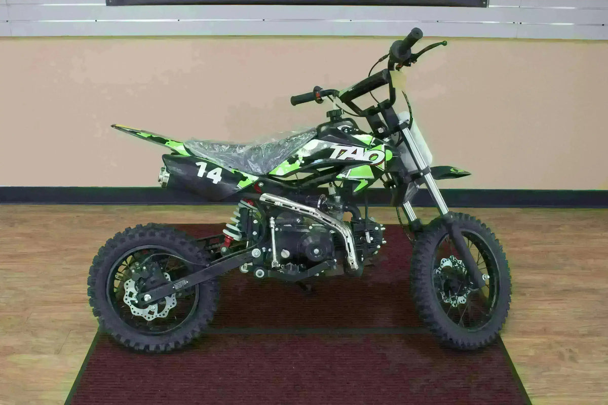 Green 110cc youth dirt bike with off-road tires and number 14 on a showroom floor