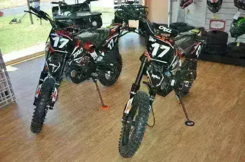 Two black and red DB17 125cc youth dirt bikes with number 17 plates displayed together in a showroom