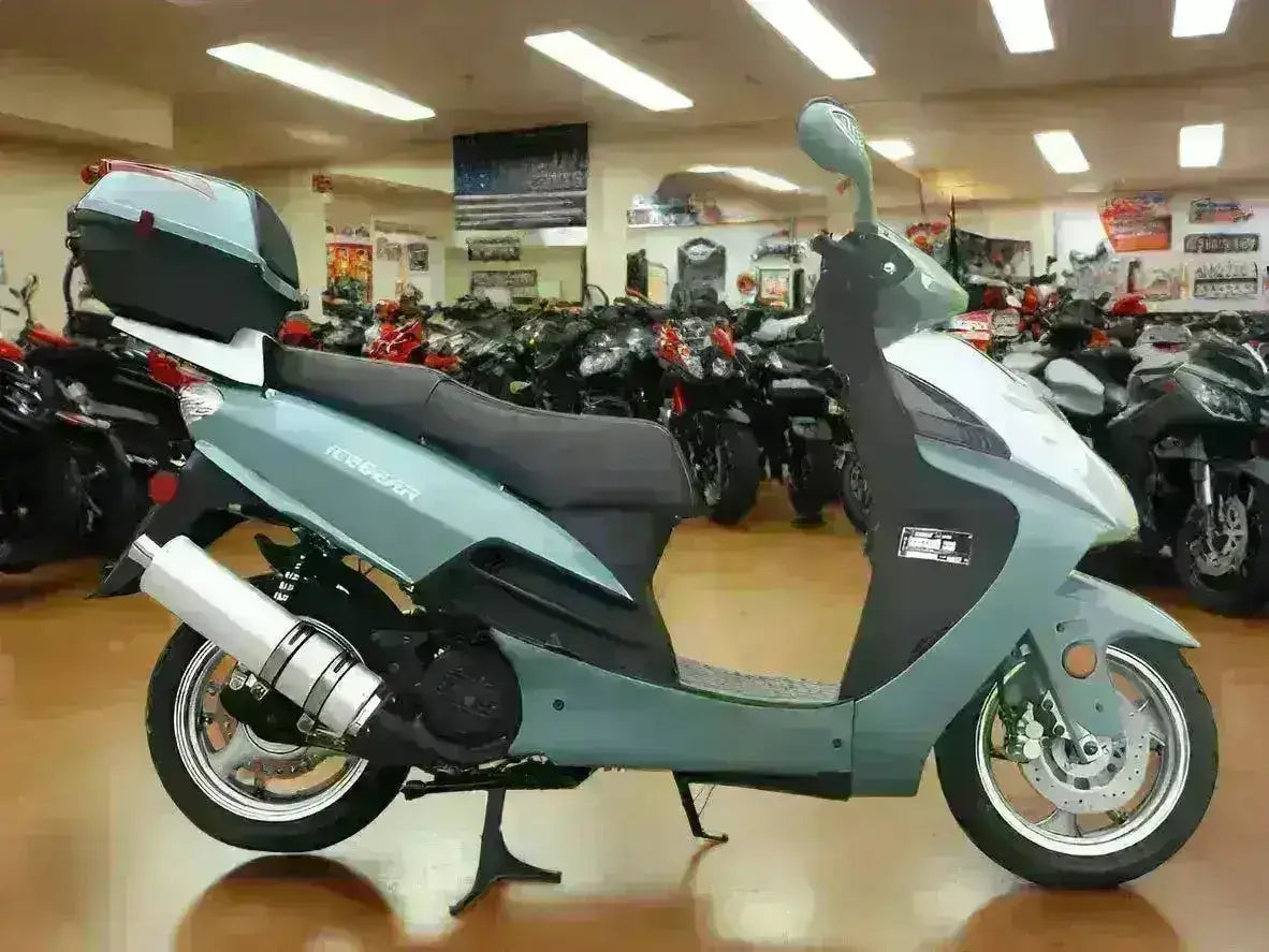 Light blue 150cc motor scooter with rear storage box displayed in showroom with motorcycles