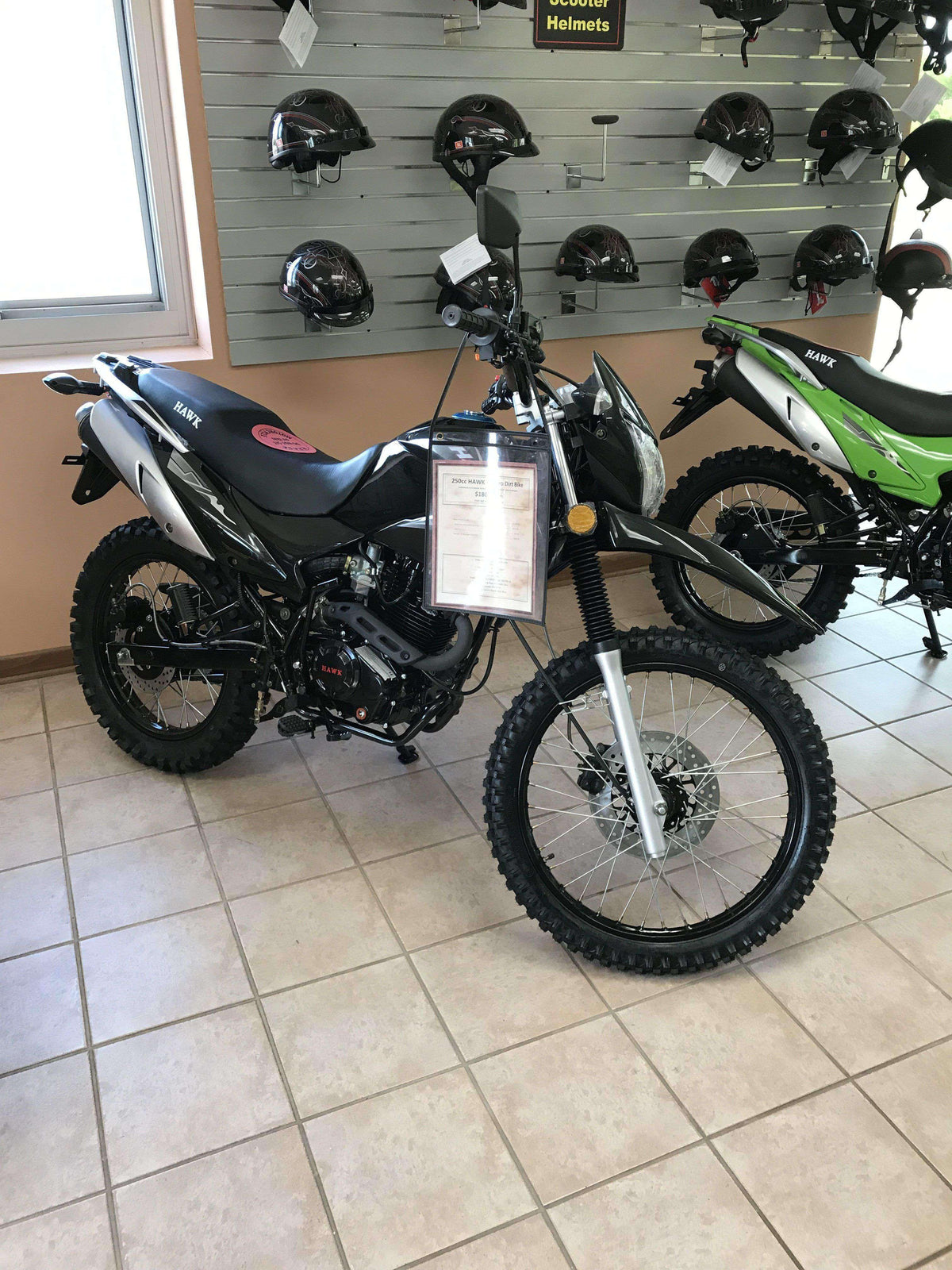 Black Hawk 250cc dirt bike with knobby tires displayed indoors near helmets