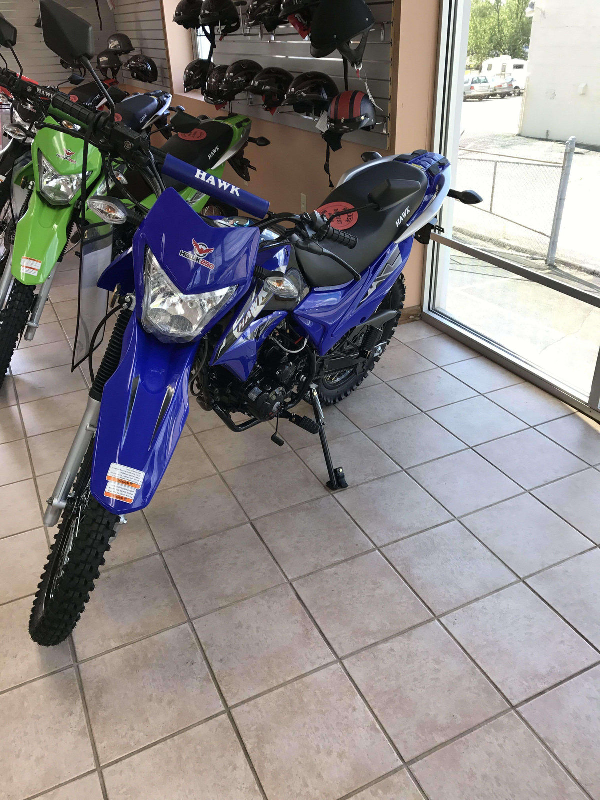 Blue Hawk 250cc dirt bike enduro on showroom floor with helmets and gear displayed