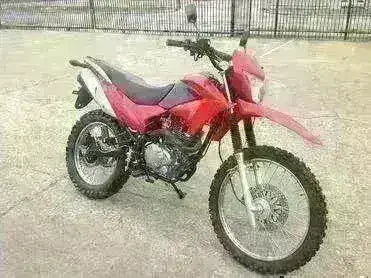 Red 250cc dirt bike parked outdoors on pavement, off-road tires, enduro style