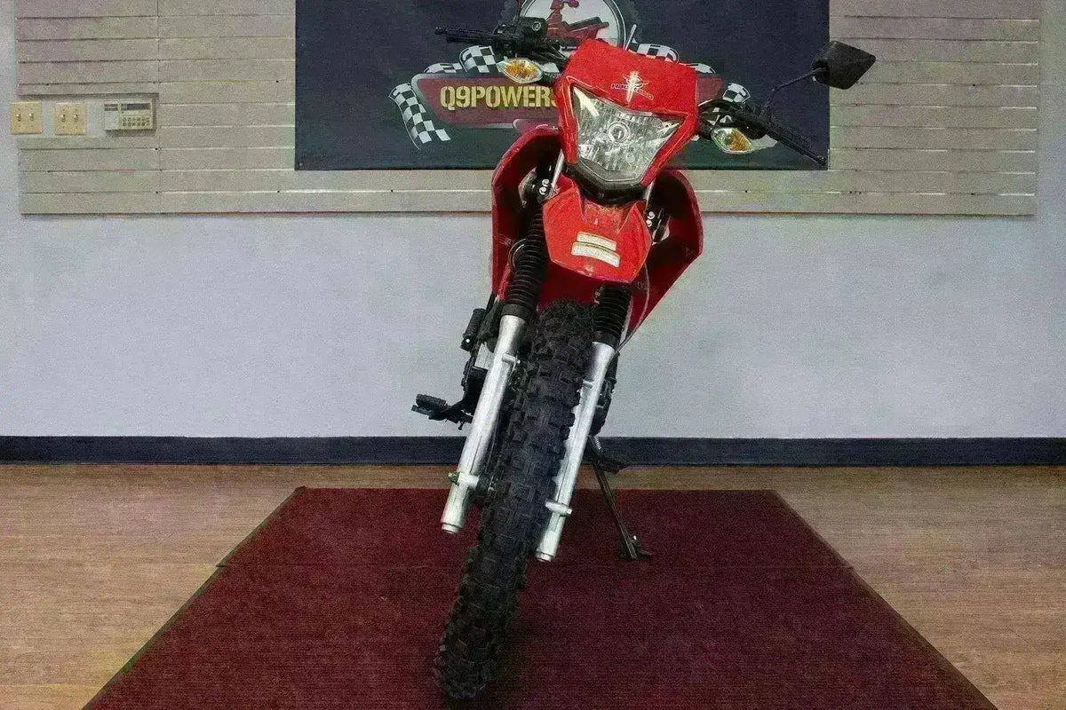 Front view of red 250cc enduro dirt bike with knobby tires indoors