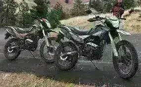 Two RPS Hawk DLX 250 dual sport motorcycles parked on roadside with trees and hills in background