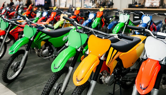 Row of colorful dirt bikes for sale in showroom, featuring green, yellow, and red models.