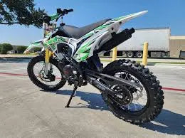 Green and white dirt bike with off-road tires parked on concrete under blue sky