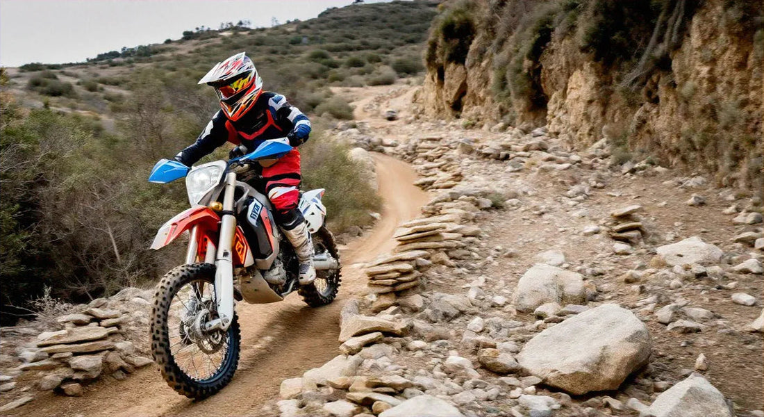 Rider in full gear on a dirt bike navigating a rocky off-road trail